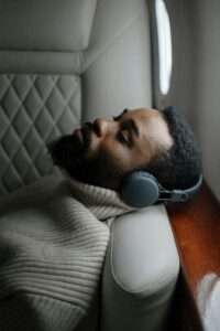 A relaxed man with wireless headphones sleeping on an airplane seat.